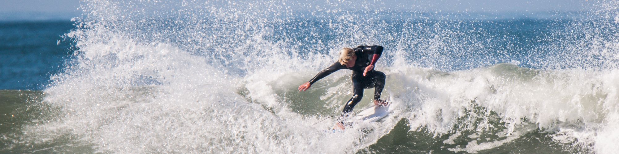 A surfer riding and performing a maneuver on a wave, with water splashing around in a dynamic display of skill over the ocean.