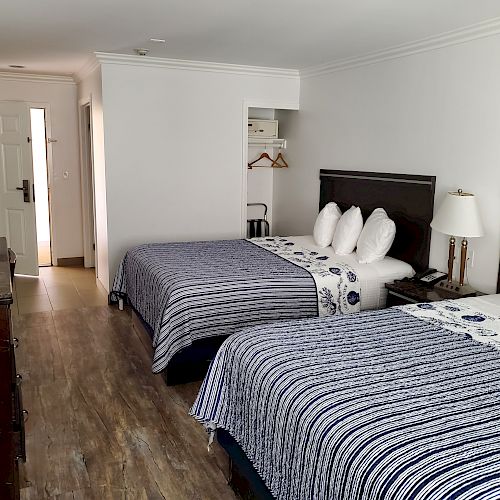 This image shows a hotel room with two double beds, dark wooden furniture, lamps, and a small closet space, featuring a clean, minimalist design.