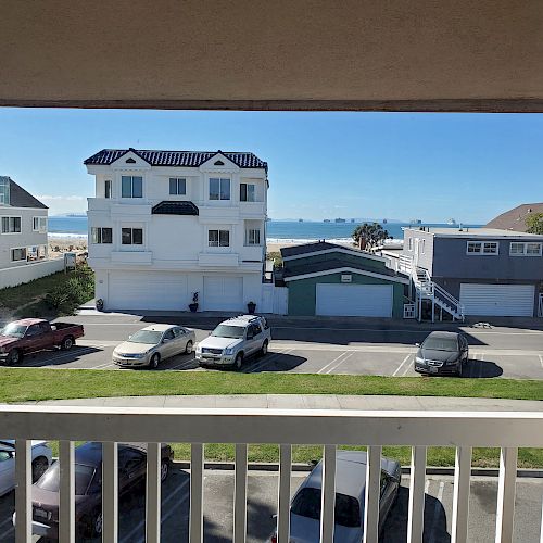 View from a balcony showing parked cars, residential buildings, and the ocean in the background on a clear day.