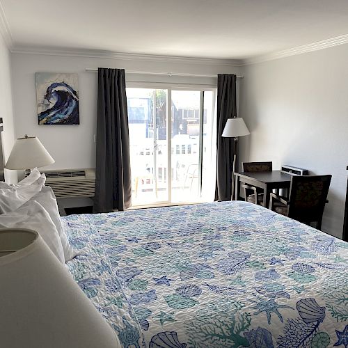 A neatly organized hotel room with a king-size bed, two lamps, a desk and chair, a mini fridge, and a sliding glass door leading to a balcony.