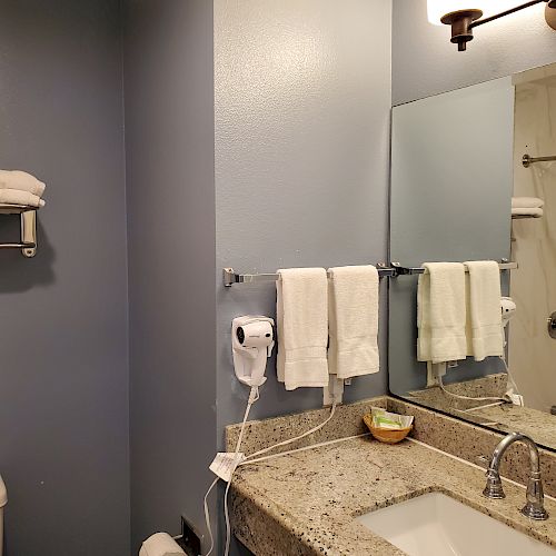 The image shows a bathroom with a sink, mirror, towels, a hairdryer, a toilet, and a towel rack with folded towels mounted on a blue wall.