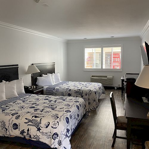 A hotel room with two double beds, desk, chair, flat-screen TV, lamps, and window, decorated with a nautical theme.