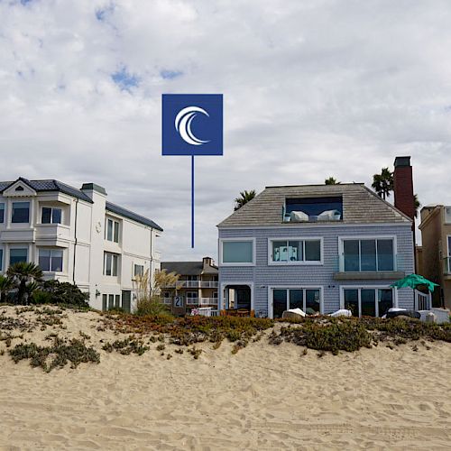 This image shows a sandy beach with three multi-story beachfront houses under a partly cloudy sky.