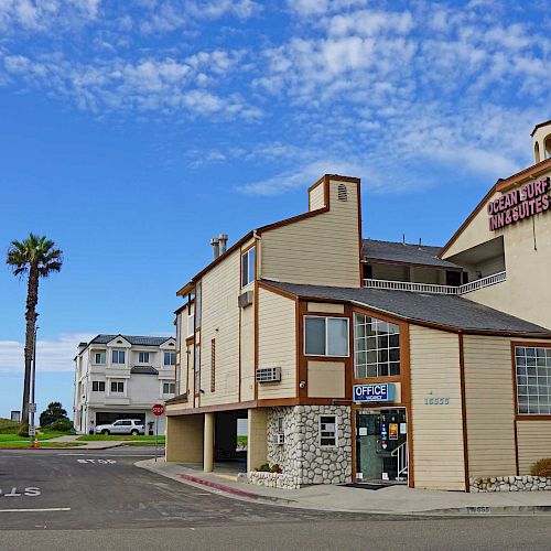 A street scene with buildings including an insurance office and a restaurant, palm trees, and houses in the background under a blue sky.