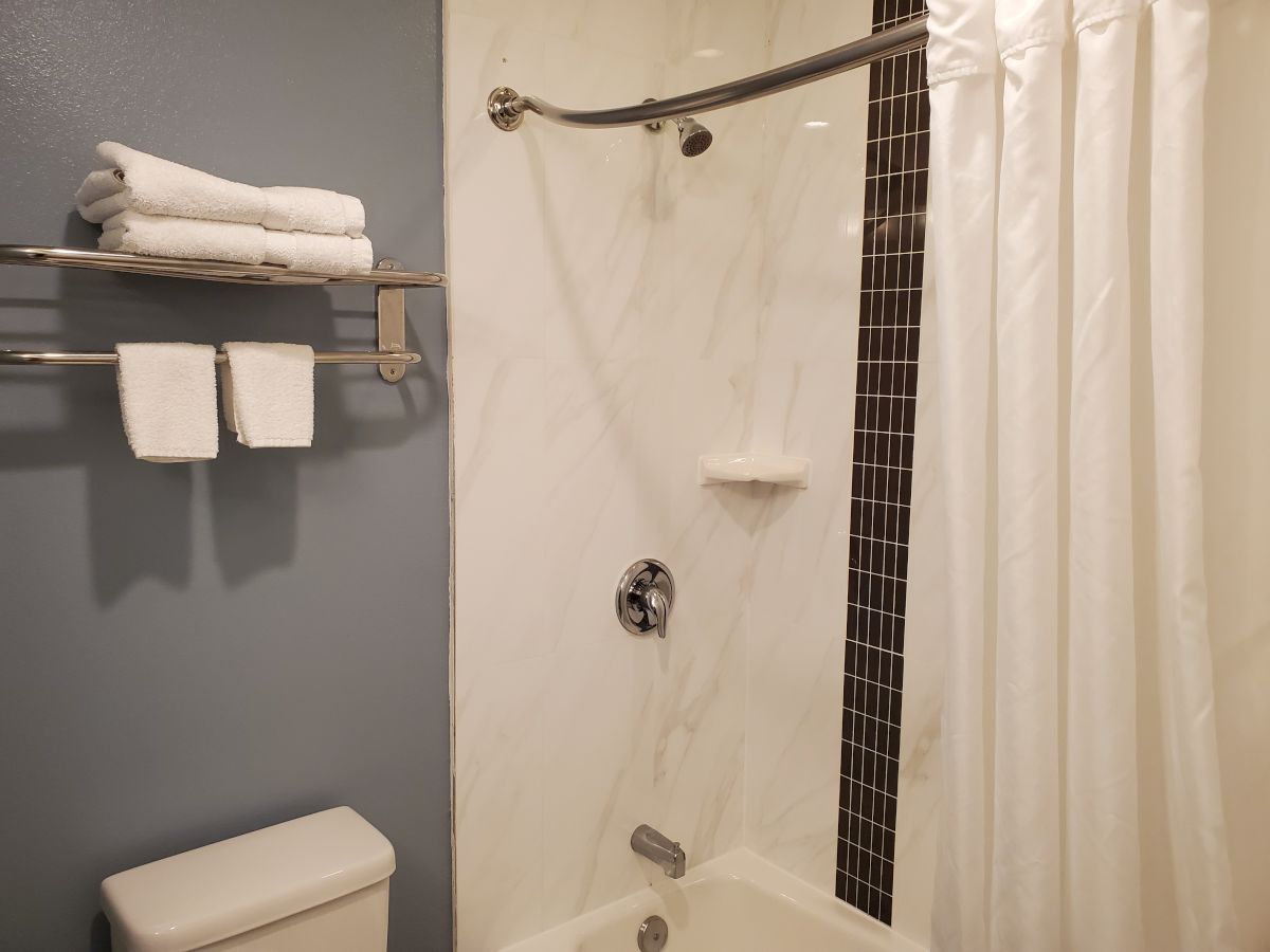 This image shows a bathroom with a white bathtub, shower curtain, silver fixtures, and a towel rack holding folded white towels on a blue wall.