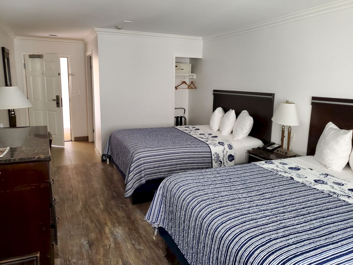 A hotel room with two double beds, a TV stand, and a small wardrobe. The room is modern with white walls and wooden flooring.