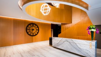 A stylish reception area with a modern design, featuring a marble desk, wooden accents, a large clock, and hanging spherical lights.