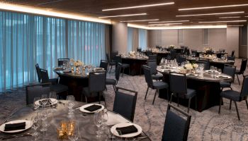 The image shows an elegantly set dining room with multiple round tables, each adorned with flowers and tableware, ready for an event.