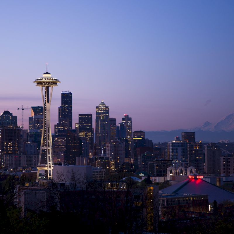 The image shows the Seattle skyline at dusk, featuring the Space Needle and various buildings with Mount Rainier visible in the background.