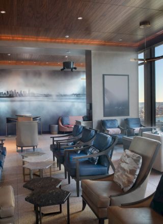 A modern lounge with comfortable seating, large windows with a scenic view of water and a Ferris wheel, and artwork on the wall.