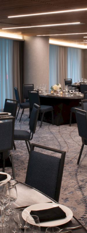 A banquet hall with round tables set for a formal event, featuring elegant table settings, black napkins, and soft lighting, with blue curtains along the wall.