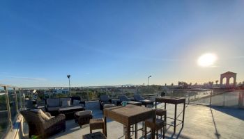 This image shows a rooftop patio with outdoor furniture, offering a clear view of a sunny sky and distant buildings, ending the sentence.